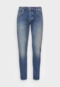 Jeans de mezclilla azul con un corte ajustado. Presenta un ligero desgastado, un lavado desteñido y bolsillos tradicionales. Cierre de botón de metal y cremallera.