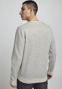 Grå teksturert hettegenser med lange ermer, rund halsutskjæring og ribbestrikkede mansjetter og kant. Laget av mykt stoff med et subtilt mønster.