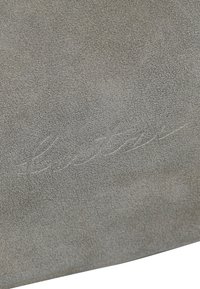 Superficie in suede grigia con una finitura texturizzata, caratterizzata da un logo goffrato sottile. Il materiale appare morbido con un aspetto opaco.