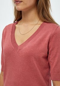 Maglione a maniche corte e scollo a V in tessuto di maglia rosa polveroso. Presenta un colletto a coste e una texture liscia. Nessun motivo o accento visibile.