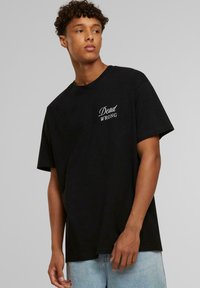 Sort bomulds T-shirt med korte ærmer, rund halsudskæring og hvid tekstgrafik "Dead WRONG" på venstre brystområde.