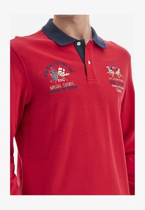 Red long-sleeve polo shirt with a navy collar, featuring embroidered designs: England National Polo Team and La Martina logos. Cotton material.