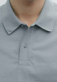 Grå polo t-shirt med en blød tekstur, der har en krave, tre-knaps knaplukning og en lomme på venstre bryst.