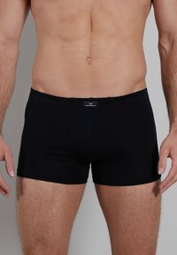 Boxer shorts noirs à coupe ajustée, fabriqués en tissu doux. Ils présentent un logo brodé sur la taille et des coutures rouges contrastantes.