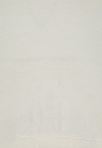 Tejido ribeteado en un tono beige claro, que presenta una textura suave y una costura uniforme a lo largo del dobladillo. No se observan patrones ni detalles adicionales.