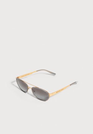 Lunettes de soleil dorées Michael Kors, avec des verres dégradés gris et une fine monture métallique, sur fond clair.