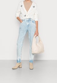 Vit stickad cardigan med blomsterbroderi, beige topp, ljusblå raka jeans med tie-dye nederkant och beige klackboots. Beigefärgad väska.