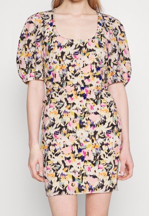 Femme portant une robe courte et ajustée avec des manches bouffantes et un motif floral abstrait coloré dans des tons rose, jaune, noir et violet.
