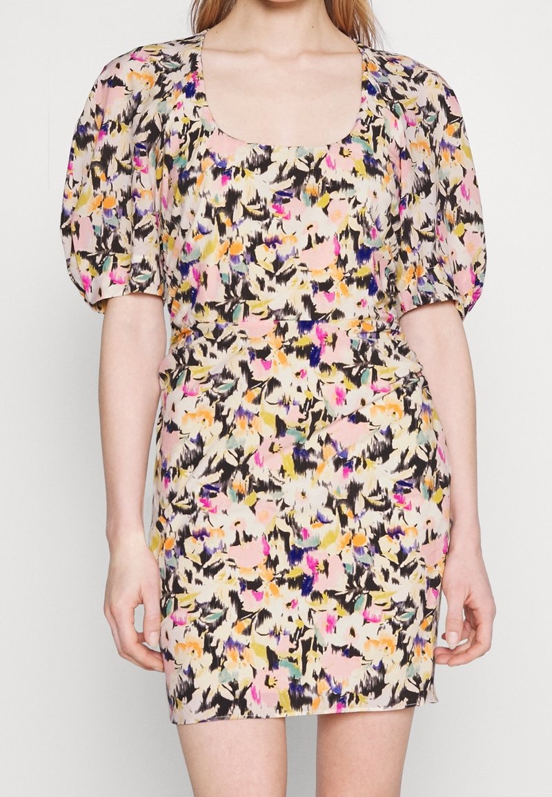 Femme portant une robe courte et ajustée avec des manches bouffantes et un motif floral abstrait coloré dans des tons rose, jaune, noir et violet.