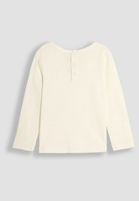 Camicia a maniche lunghe di colore crema con scollatura rotonda e patta con bottoni sul retro. Texture liscia senza motivi visibili.