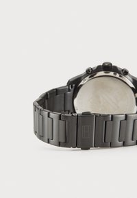 Svart rustfritt ståluhr med en polert sølvfarget bezel, lenkearmbånddesign, synlig lås og et gravert logo på remmen.