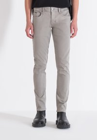 Jeans ajustados de denim en gris claro, con una textura sutil, cinco bolsillos y cierre de botón, combinados con botines negros.