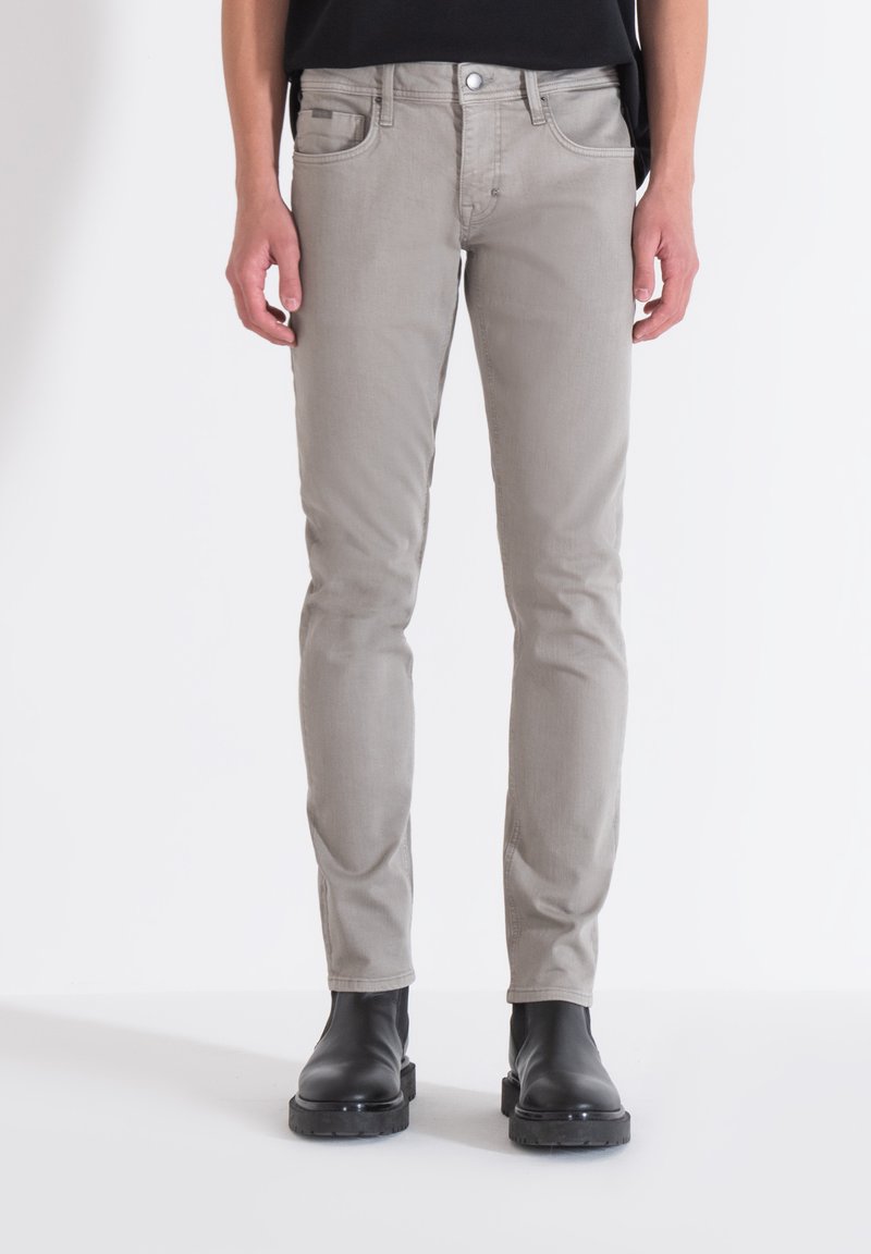 Jeans ajustados de denim en gris claro, con una textura sutil, cinco bolsillos y cierre de botón, combinados con botines negros.