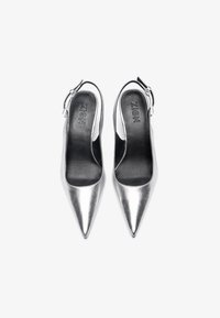 Hopeiset, teräväkärkiset slingback-kengät mustilla sisäpohjilla ja säädettävillä nilkkahihnoilla, esitelty vierekkäin valkoista taustaa vasten.