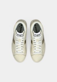 Une paire de baskets Diadora blanches et beiges avec des lacets blancs, vue de dessus sur un fond clair.