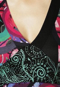 Lähikuva V-kaula-aukollisesta vaatteesta, jossa on päällekkäisiä kangaspaneeleja, joissa on värikkäitä kukka- ja abstrakteja musta-teal paisley -kuvioita.