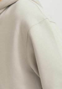 Light taupe hoodie with a textured, soft fabric. Features a regular fit, ribbed cuffs, and visible stitching details along the shoulder seam.