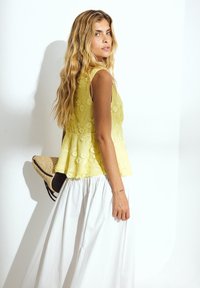 Yellow floral lace top with a peplum design, paired with a white flowing skirt. Model holds a straw hat, showcasing a textured fabric.
