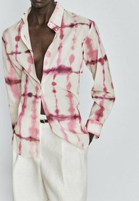 Lichte button-up shirt van een fijne stof, met een roze en bruine tie-dye patroon, open kraag en lange mouwen. Gecombineerd met crèmekleurige broeken.