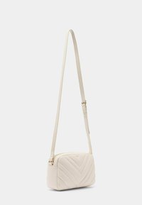 Crossbody-väska i mjuk beige konstläder, med chevron-quiltad struktur, smal justerbar rem och detaljer i guldfärg.