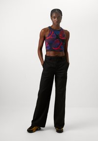 Črni top brez rokavov s pisanim motivom vrtnic, kombiniran z ohlapnimi črnimi hlačami in črnimi supergami z rumenimi poudarki.