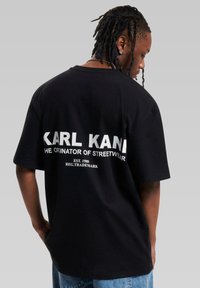 Black cotton t-shirt featuring bold white text on the back: "KARL KANI THE ORIGINATOR OF STREETWEAR," with a relaxed fit and short sleeves.