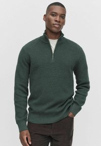Ciemnozielony sweter dzianinowy z wysokim kołnierzem i półzamkiem. Żebrowana struktura i dopasowane rękawy. Noszony na lekko koszuli.