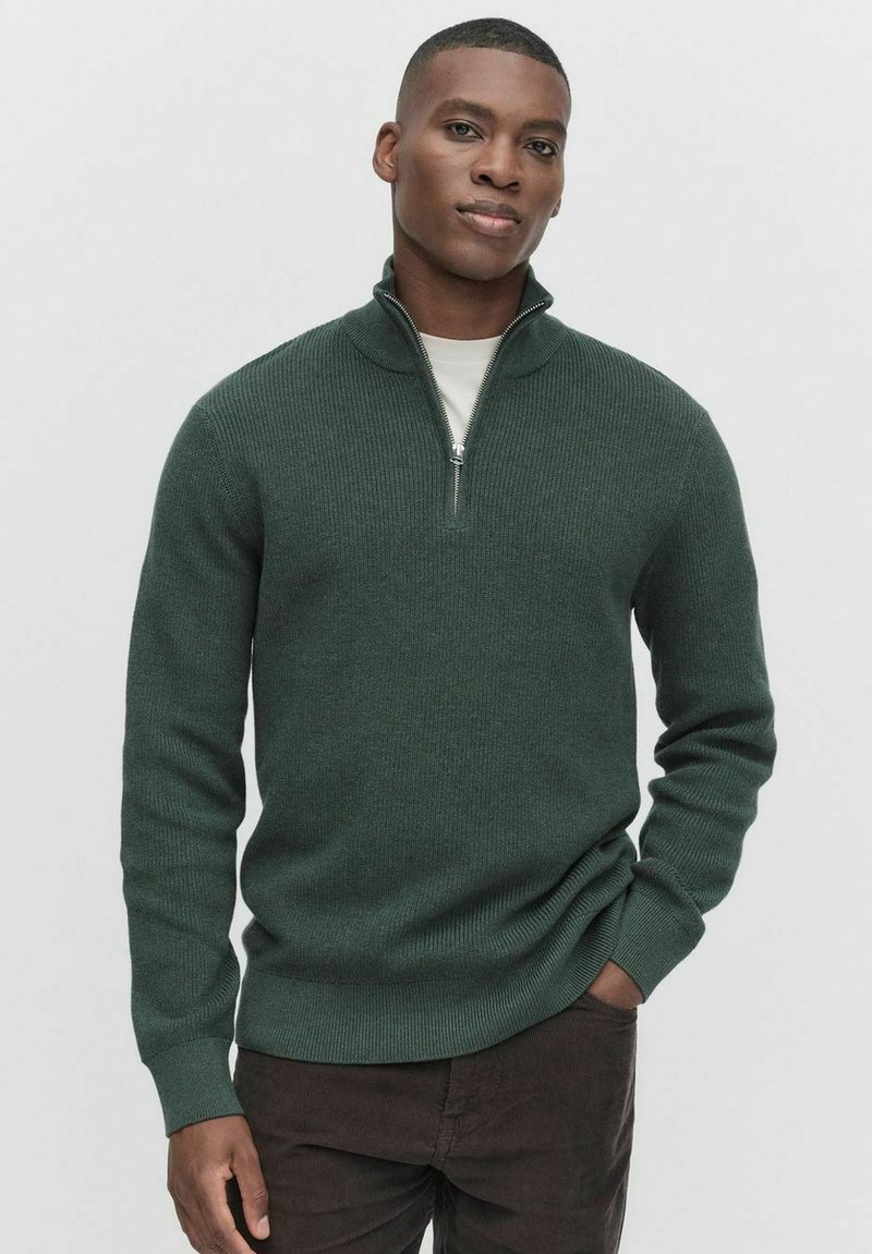 Ciemnozielony sweter dzianinowy z wysokim kołnierzem i półzamkiem. Żebrowana struktura i dopasowane rękawy. Noszony na lekko koszuli.