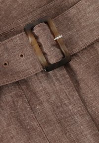 Ceinture en tissu marron avec une boucle rectangulaire en écaille de tortue passée dans l'une des trois boutonnières visibles sur un vêtement texturé.