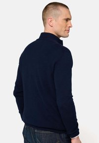 Pull en coton bleu marine avec col montant, poignets côtelés et texture lisse, vu de dos, associé à un jean en denim foncé.