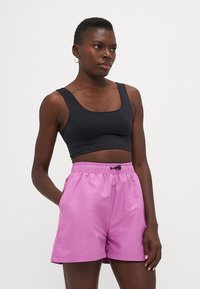 Črn prilegajoč se športni crop top in rozaste široke kratke hlače z elastičnim pasom in detajlom vrvice, izdelane iz gladkega, lahkega materiala.