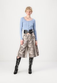 Plava rebrasta majica dugih rukava s detaljima na gumbima, u kombinaciji s uzorcima hlačama culottes u piton printu i crnim čizmama do koljena s bijelim vezom.