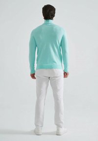 Pull en maille vert menthe léger, avec un col montant et des poignets côtelés, associé à un pantalon blanc slim et des baskets.
