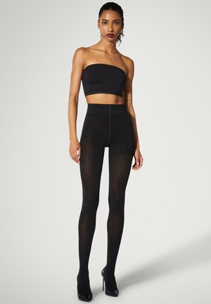 Leggings nere con motivo a rombi testurizzato e vita alta, abbinati a un top nero senza spalline e tacchi alti.