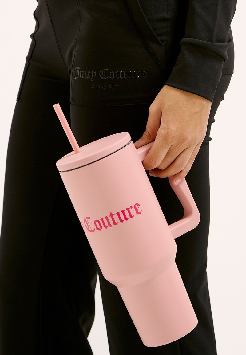Conteneur à boisson rose avec une poignée, une paille et un couvercle noir contrasté. Présente le texte en gras "Couture" en rose. Fini lisse et mat.