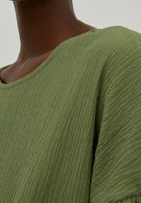 Vihreä, teksturoitu paita pyöreällä pääntiellä, jossa on pehmeä, ribsikuvio. Kangas on kevyt ja rento istuvuus.