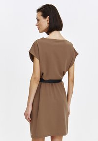Brązowa sukienka z krótkimi, szerokimi rękawami, lekko luźnym fasonem i czarnym paskiem podkreślającym talię. Gładki materiał z minimalnymi detalami.