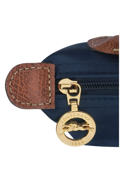 Navy fabric pouch with a textured brown leather flap, featuring a gold zip with a round logo charm marked "LONGCHAMP 1948."