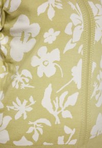 Kurzärmliges, hellgrünes Oberteil mit einem weißen Blumenmuster, glatter Textur und einer zentralen Naht mit sichtbaren Stichdetails.
