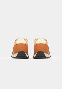 Baskets en suède orange et beige avec une semelle en caoutchouc, dotées d'un talon rembourré et d'un design minimaliste. Couture détaillée sur le dessus.