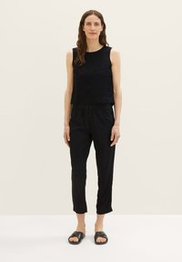 Zwarte mouwloze top gecombineerd met zwarte drawstringbroek, met een relaxte fit. Draagt met minimalistische zwarte sandalen. Vlotte textuur.