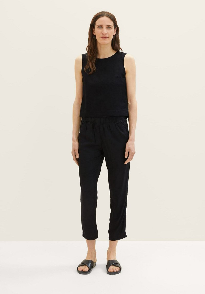 Zwarte mouwloze top gecombineerd met zwarte drawstringbroek, met een relaxte fit. Draagt met minimalistische zwarte sandalen. Vlotte textuur.