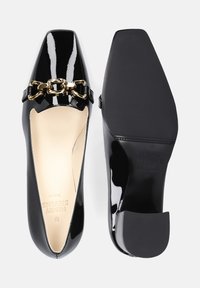 Scarpe in pelle verniciata nera con punta affusolata, decorate con una catena dorata e un tacco basso a blocco. Interno liscio e suola testurizzata.