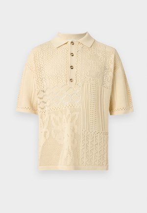 Kremfarvet kortærmet strikket poloshirt med mønstret hulmønster og fire brune knapper på stolpen.