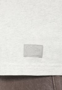 Ανοιχτό γκρι βαμβακερό t-shirt με ανάγλυφη, ανάγλυφη ετικέτα λογότυπου Vans στο κάτω μέρος. Λεπτή υφή, με καλοραμμένο τελείωμα πάνω από σκούρο ύφασμα.