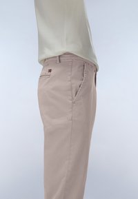 Pantaloni beige chiaro con design a gamba dritta, dotati di una tasca laterale e un piccolo dettaglio a bandiera sulla tasca posteriore. Texture di cotone morbido.