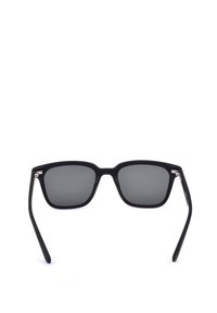 Lunettes de soleil noires à monture carrée avec verres foncés et branches légèrement incurvées sur fond blanc.