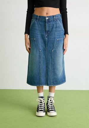 Fustă midi din denim, cu buzunare frontale și croială dreaptă, realizată dintr-un material albastru deschis, cu detalii de cusături vizibile. Asortată cu adidași închisi la culoare.