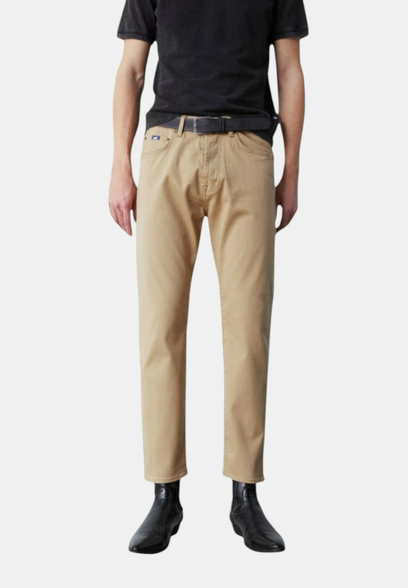 Pantaloni in cotone beige con vestibilità dritta e leggermente affusolata. Presentano tasche frontali e una cintura. Abbinati a stivaletti neri alla caviglia.