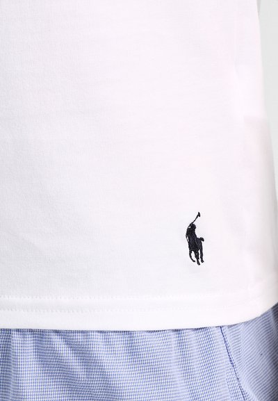 T-shirt en coton blanc avec un col rond, présentant un petit logo de poney noir brodé sur le bas à gauche. Tissu texturé.